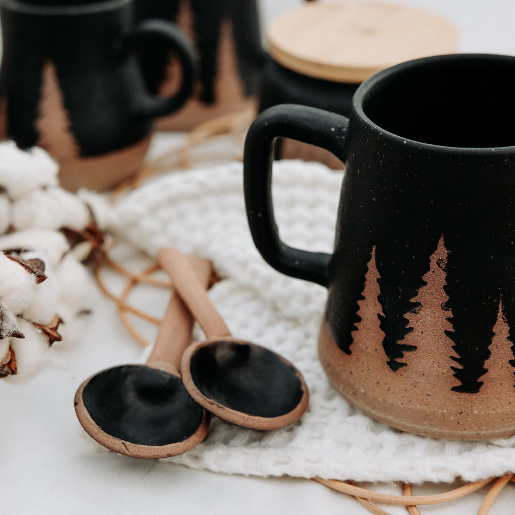 Black and tan mug with the outline of evergreen trees.
